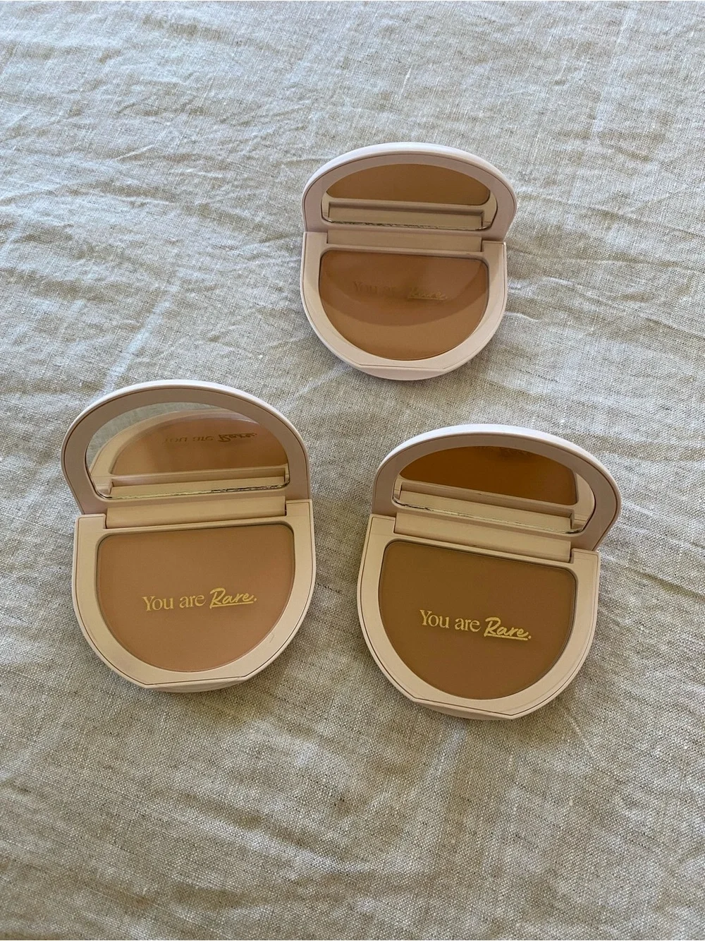 Rare Beauty pressed powder compacts in warm beige and tan tones